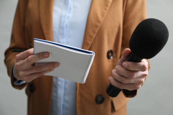 Journalist with microphone and notebook on grey background, closeup