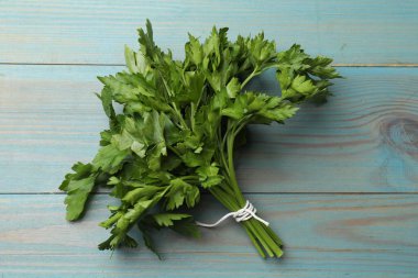 Açık mavi ahşap masada bir demet taze maydanoz.