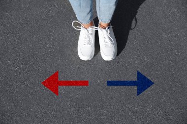 Kırmızı ve mavi okların yanında duran kadın asfalt yolda farklı yönleri işaret ediyor, yakın plan. Seçim, karar, alternatif yol kavramları