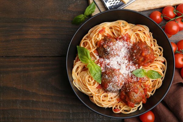 Вкусная паста с фрикадельками в миске и помидорами на деревянном столе, плоский уголок. Пространство для текста
