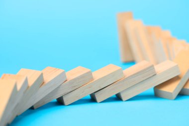 Domino etkisi. Tahta bloklar açık mavi arkaplan üzerine düşüyor, yakın plan