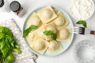 Beyaz fayanslı masada servis edilen peynirli ve fesleğenli lezzetli ravioli.