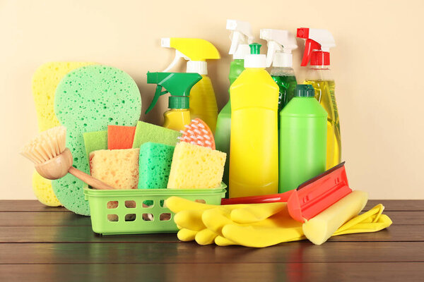 Различные чистящие средства и материалы на деревянном столе на бежевом фоне