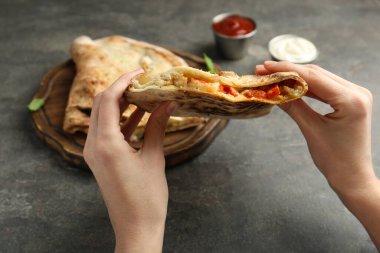 Gri desenli masada etli, peynirli ve domatesli leziz calzone yiyen kadın, yakın plan.