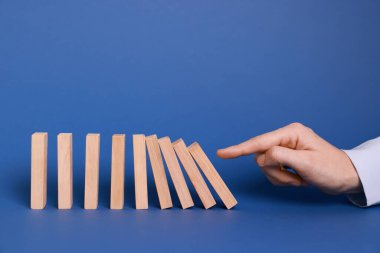 Domino etkisi. Mavi arka planda tahta blokları iten kadın, yakın plan