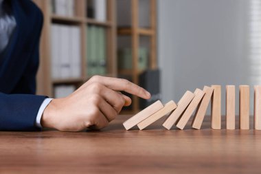 Domino etkisi. Masada tahta blokları iten adam, yakın plan.