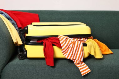 İçerideki kanepede farklı kıyafetlerle dolu parlak bavul.