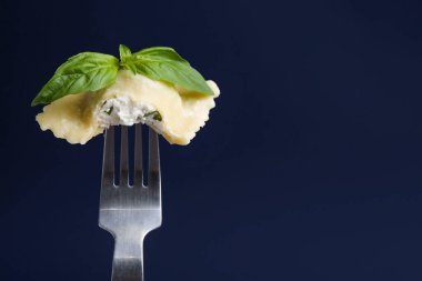 Koyu mavi arka planda peynirli ve fesleğenli lezzetli ravioli, yakın plan. Metin için boşluk