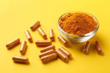 Kasedeki zerdeçal tozu ve sarı arka plandaki kapsüller, yakın plan.