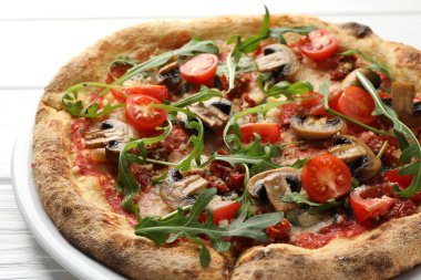 Beyaz ahşap masada mantarlı, domatesli ve roka aromalı lezzetli pizza.