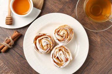 Taze pişmiş elma gülleri, bal, tarçın çubukları ve ahşap masada çay.