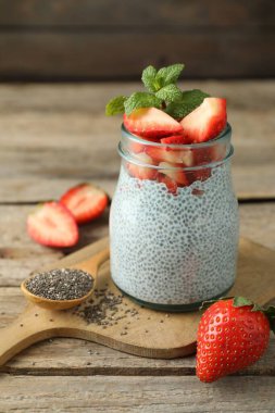 Çilekli lezzetli chia pudingi ve ahşap masada cam kavanozda naneli şeker.