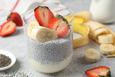 Çilekli lezzetli chia pudingi ve açık gri masada muz, yakın plan.