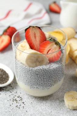 Çilekli lezzetli chia pudingi ve açık gri masada muz, yakın plan.