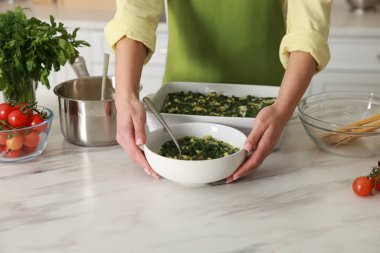 İçerideki mermer masada ıspanaklı lazanya yapan kadın, yakın plan.