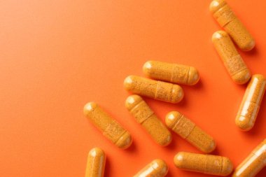 Turuncu arka planda zerdeçal kapsülleri, üst manzara. Metin için boşluk