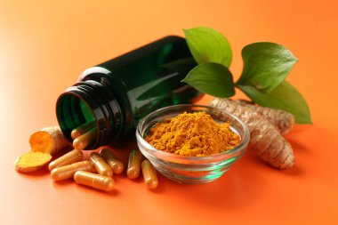 Kavanozda zerdeçal tozu, kapsüller ve turuncu arka planda kökler, yakın plan