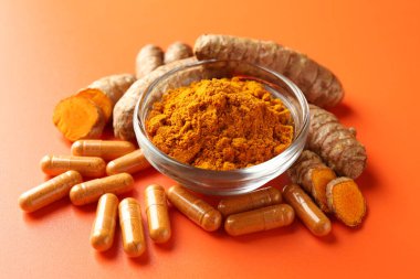 Kavanozda zerdeçal tozu, turuncu arka planda kök ve kapsüller, yakın plan.