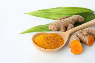 Kaşıkta zerdeçal tozu, beyaz arka planda yeşil yapraklar ve kökler, yakın plan. Metin için boşluk