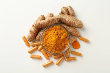 Beyaz zemin üzerinde zerdeçal kapsülleri, toz ve kökler düz yatıyordu