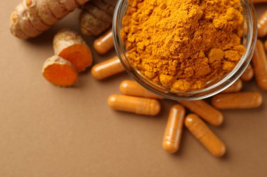 Zerdeçal kapsülleri, toz ve kökler bej arka planda, düz yerde. Metin için boşluk