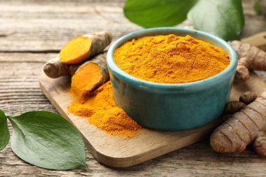 Tabakta zerdeçal tozu, kökler ve yapraklar ahşap masada, yakın plan.