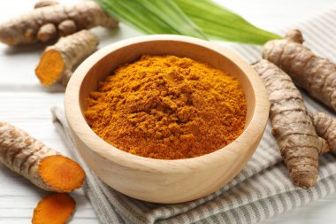 Aromatik zerdeçal tozu, taze kökler ve beyaz ahşap masa üzerindeki yapraklar, yakın plan.