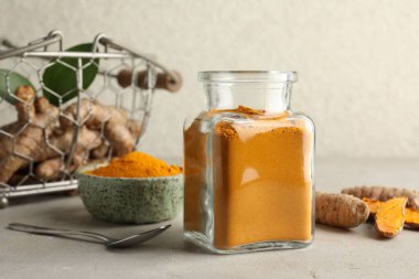 Cam kavanozda Aromatik zerdeçal tozu ve açık gri masada taze kökler.