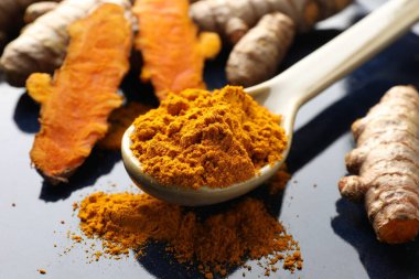 Kaşıkta aromatik zerdeçal tozu ve mavi tabakta taze kökler, yakın plan.