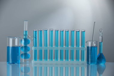 Aynanın yüzeyinde gri arka planda mavi sıvı bulunan laboratuvar camları