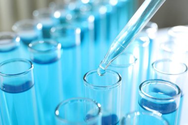 Işık arkaplanındaki test tüplerine sıvı damlatılıyor.