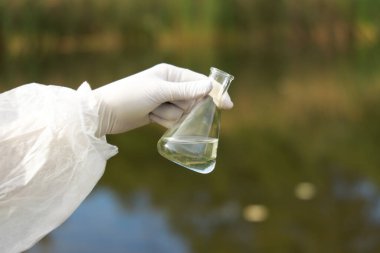 Su kalitesinin incelenmesi. Araştırmacı elinde numune olan bir şişe tutuyor, yakın plan.