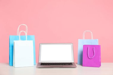 İnternet alışverişi. Laptop ve renkli kese kağıtları pembe arka planda.