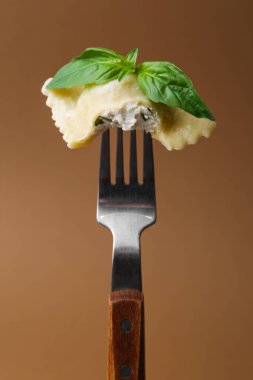 Peynirli ve fesleğenli lezzetli ravioli kahverengi arka planda, yakın plan.