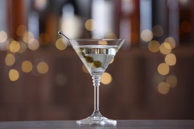 Arkaplanı bulanık olan, ahşap masadaki zeytinli martini kokteyli. Bokeh etkisi