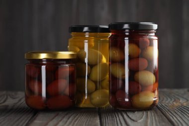 Cam kavanozlarda zeytin turşusu. Ahşap masada, gri arka planda.