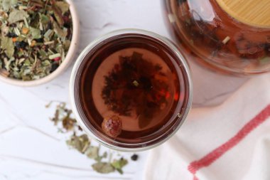 Lezzetli bitkisel çay ve kuru yapraklar beyaz masada, düz yerde.