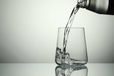 Açık gri arka planda şişeden bardağa ferahlatıcı soda dökülüyor, yakın plan. Metin için boşluk