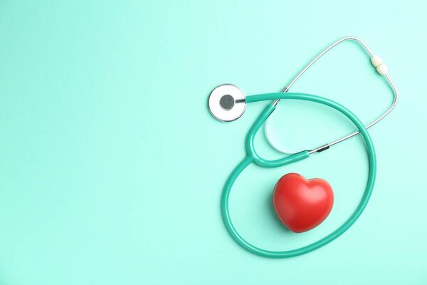 Cardiology. Stethoscope and red decorative heart on turquoise background, flat lay. Space for text
