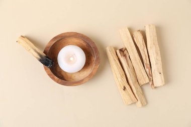 Palo santo çubukları, yanmış bir tane ve bej arka planda yanan bir mum, düz uzanmış