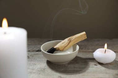 Yanan palo santo sopa ve yanan mumlar ahşap masa karşı gri arka plan, yakın çekim