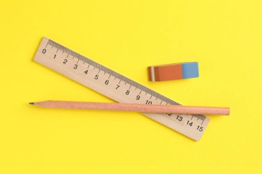 Sarı arka planda cetvel, kalem ve silgi düz.