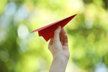 Bulanık yeşil arka planda el yapımı kağıt uçaklı kadın, yakın plan.