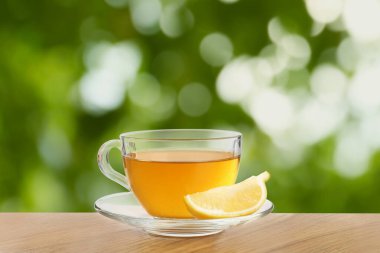 Yeşil çay fincanda ve limon dilimi dışarıda, ahşap masada.