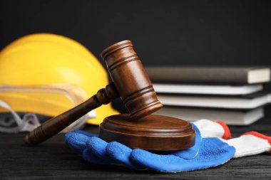 İş yerinde kaza oldu. Gavel, kitaplar ve inşaat işçilerinin koruyucu giysileri siyah ahşap masada, seçici odaklı.