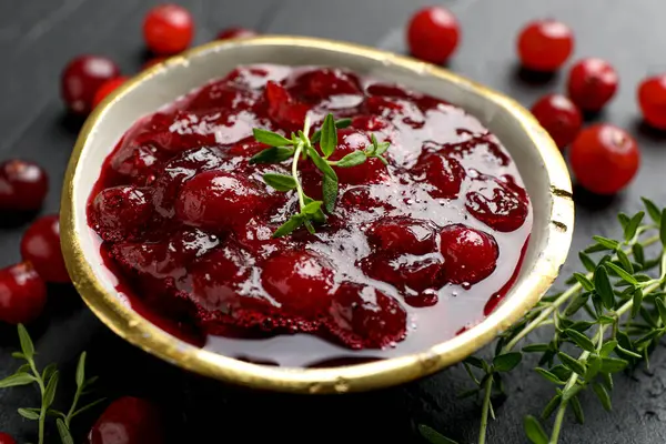 Lezzetli kızılcık sosu kasede, böğürtlen ve kekik siyah masada, yakın plan.