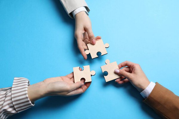 Business strategy and teamwork concept. Partners with different puzzle pieces on light blue background, top view