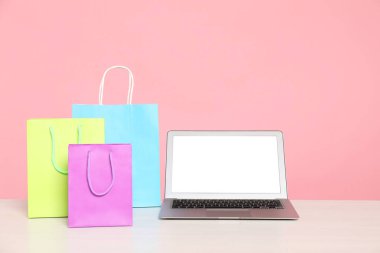 İnternet alışverişi. Laptop ve renkli kese kağıtları pembe arka planda.