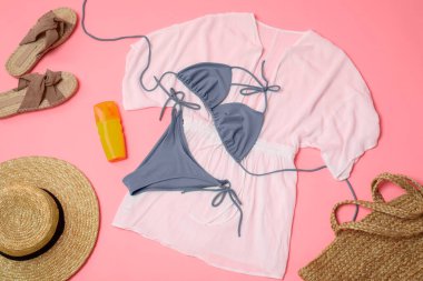 Pembe arka planda şık mayo, güneş kremi ve plaj aksesuarları, düz uzanma