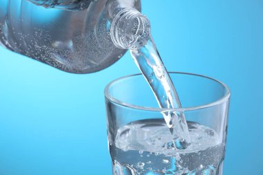 Açık mavi arkaplanda şişeden cama taze soda dökülüyor, yakın plan.